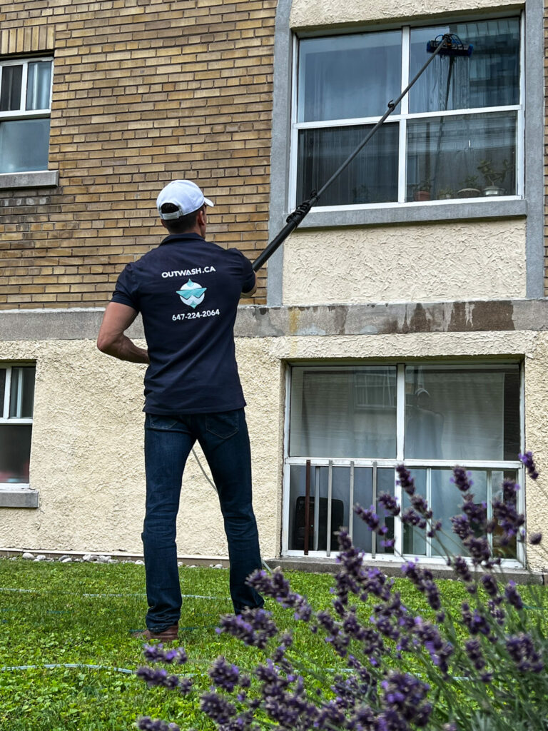 Expert window cleaner using a Water Fed Pole connected to a 4-stage water purification system to clean the windows of a multi-story building, with vibrant flowers in the foreground.