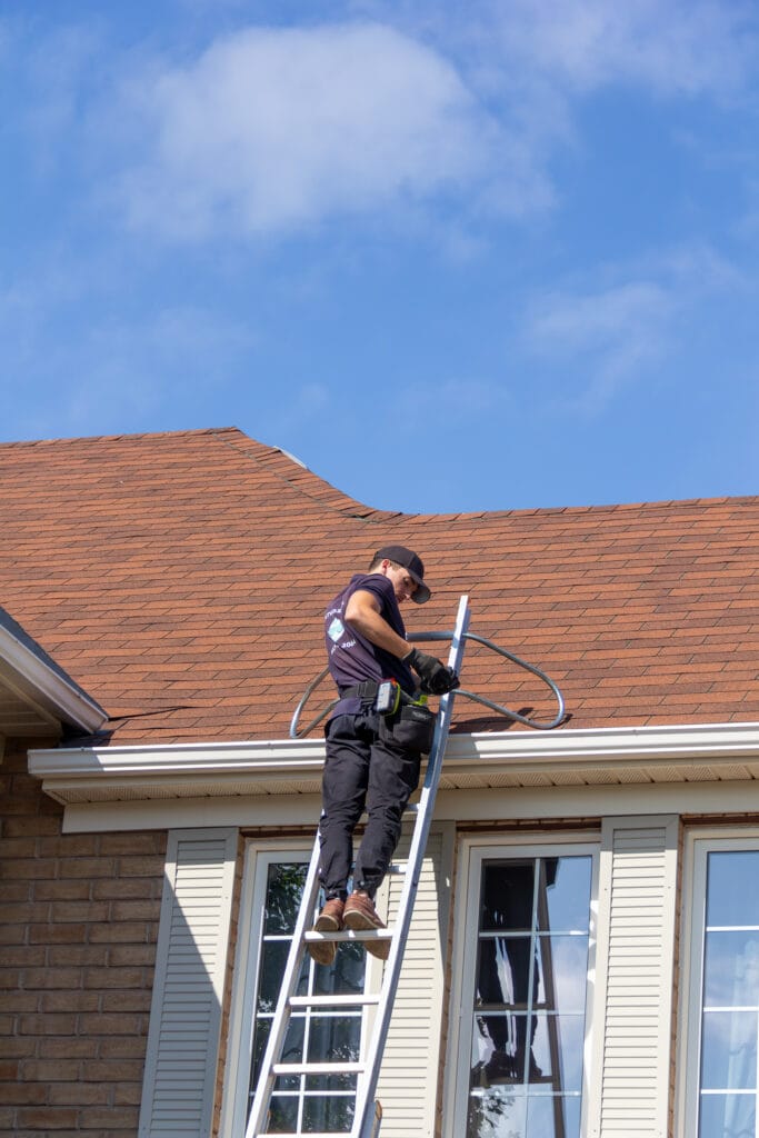 Outwash technician on a ladder at the roof edge of a house