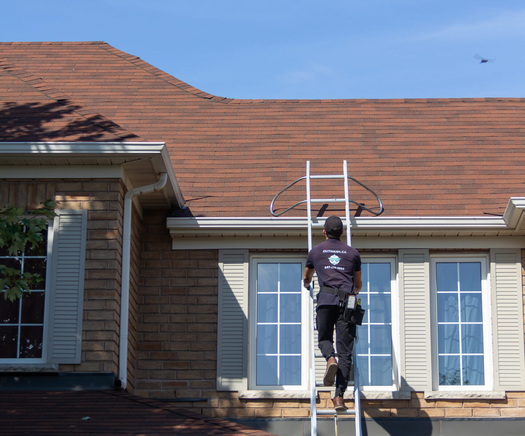 OutWash technician on ladder inspecting and cleaning gutters on a two-story brick house in Toronto