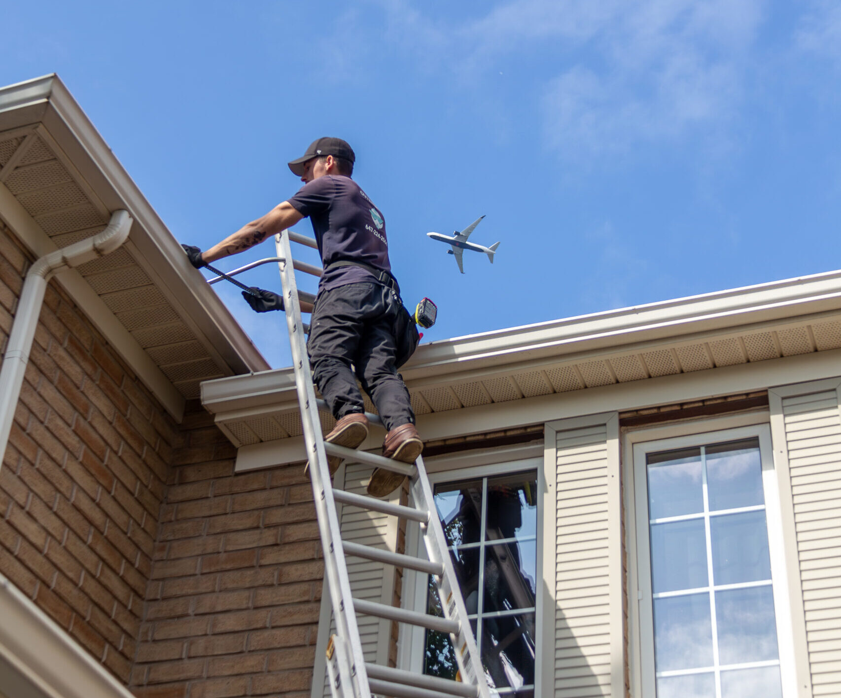 Technician on ladder cleaning gutters of a two-story brick house for OutWash in Toronto