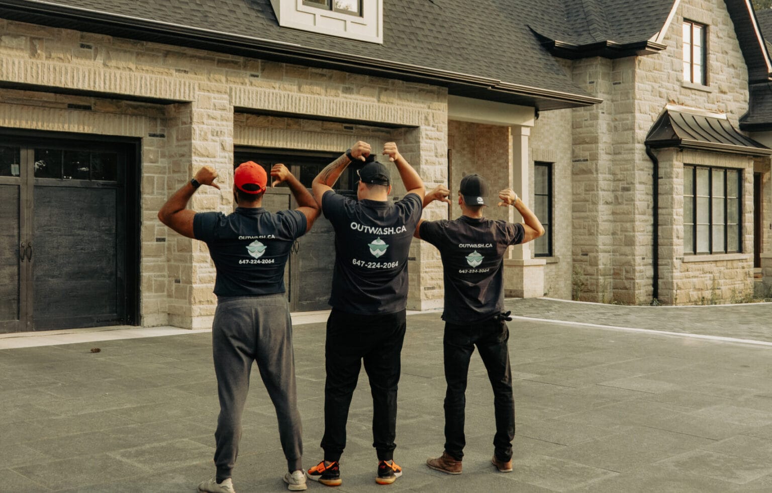 Three Outwash crew members, seen from behind, flexing in front of a house
