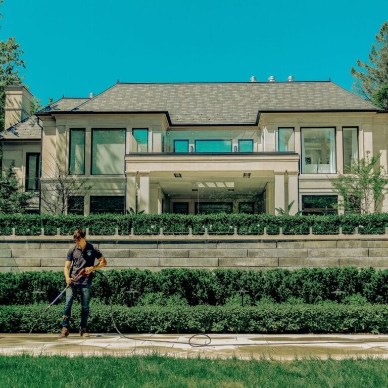 Outwash technician pressure washing in front of a large house