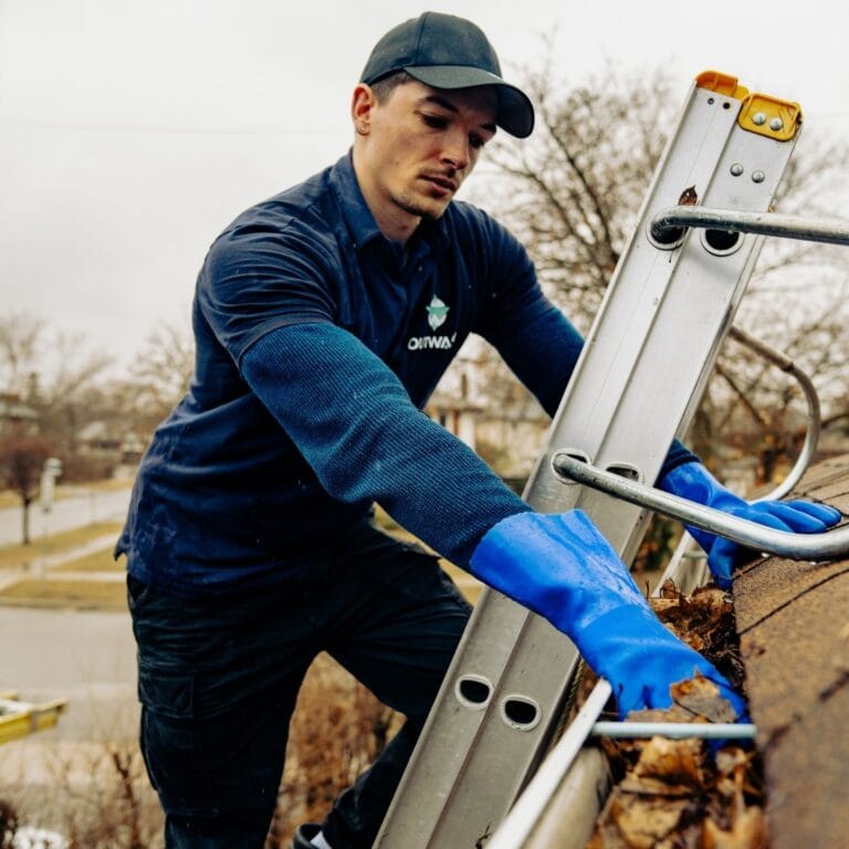Outwash technician on a ladder clearing a gutter