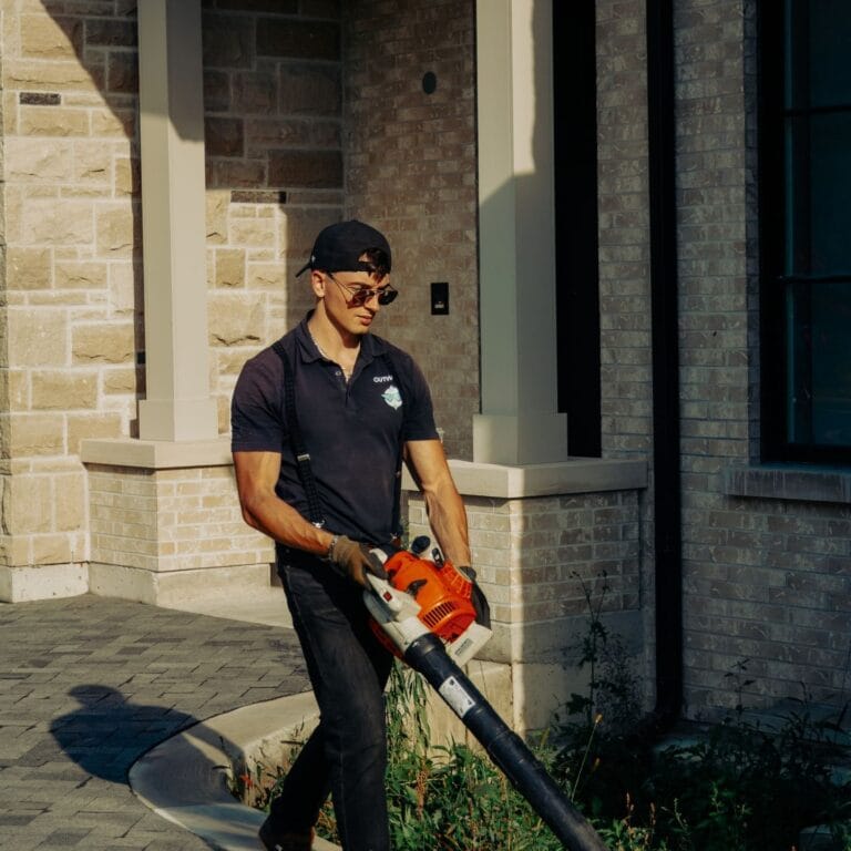 Outwash technician with a leaf blower beside a stone house