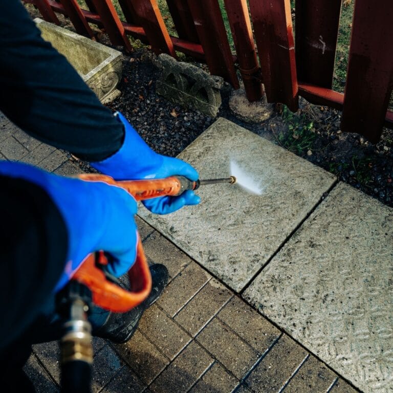 Gloved hands holding a pressure washer over paving stones
