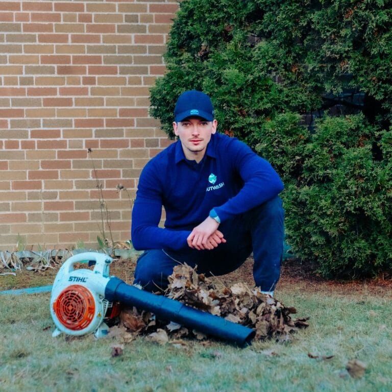 Outwash technician crouching beside a leaf blower and a pile of leaves