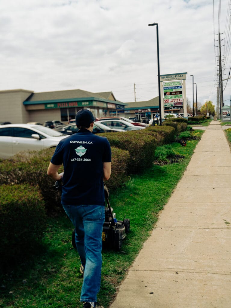 Outwash technician mowing along a hedge at a retail plaza