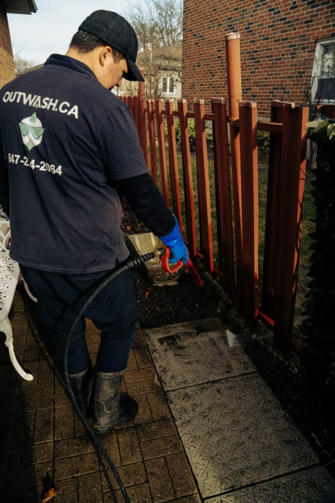 Outwash technician pressure washing a walkway beside a wooden fence