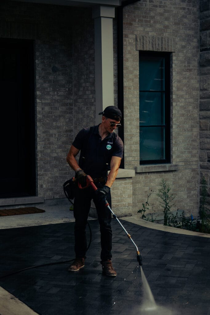 Outwash technician pressure washing a dark paved driveway