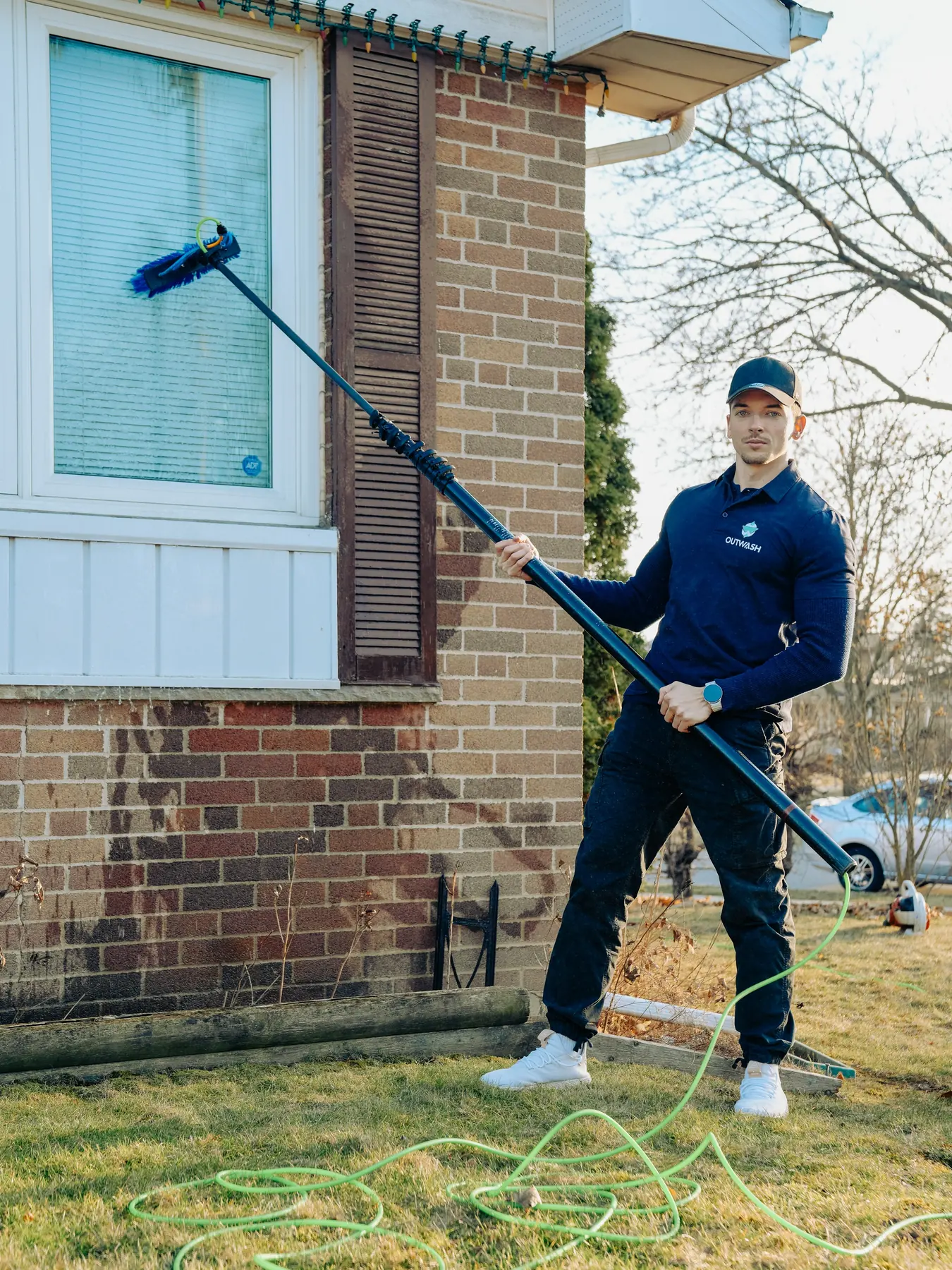 Outwash technician holding a water-fed pole at the window of a brick house