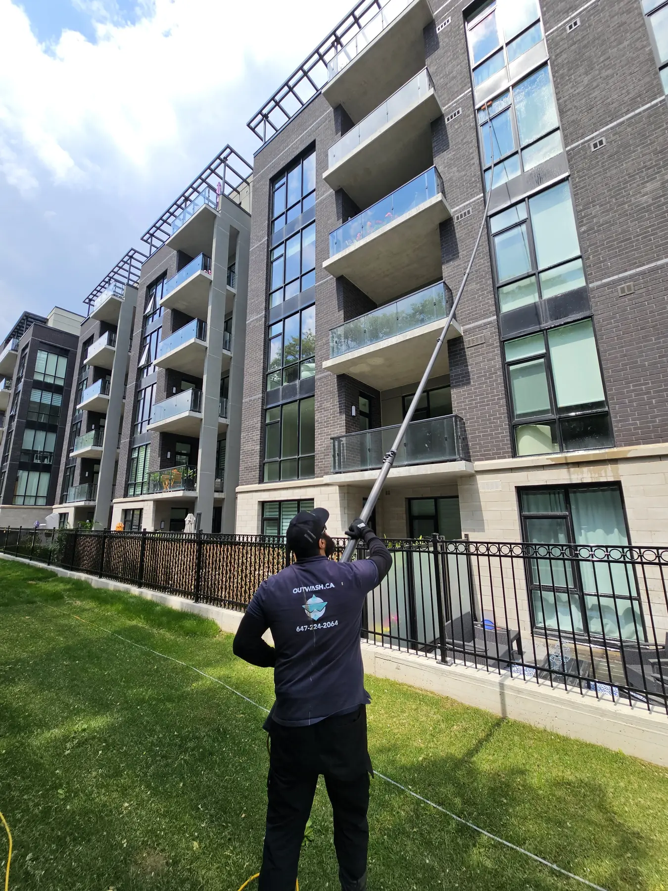 Outwash technician cleaning the upper windows of a condo building with a water-fed pole
