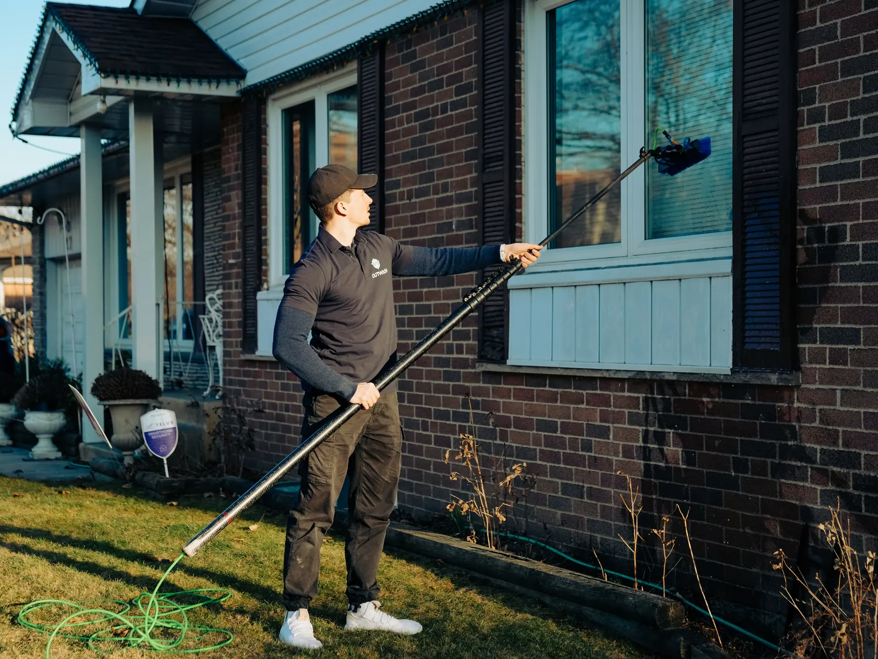 Outwash technician cleaning the window of a brick house with a water-fed pole