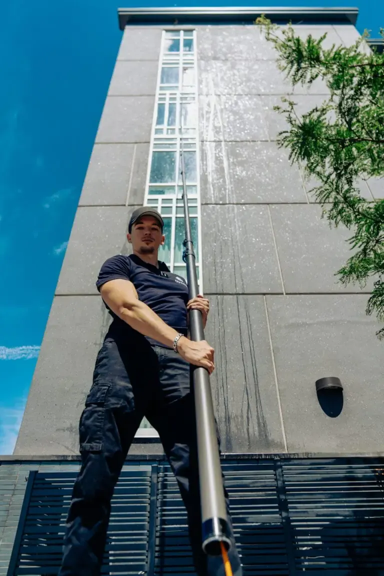Outwash technician cleaning the windows of a tall building with a water-fed pole