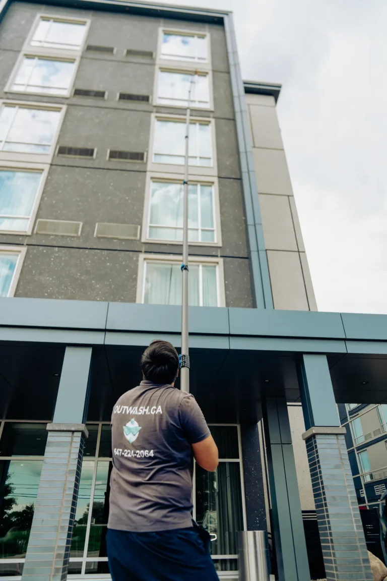 Outwash technician cleaning upper-floor windows with a water-fed pole